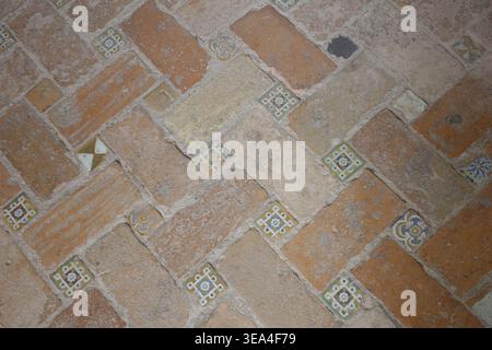 Ancient herringbone terracotta floor with decorative hand-painted ceramic tile inlays featuring Moorish floral motifs, Alhambra, Granada, Spain. Stock Photo