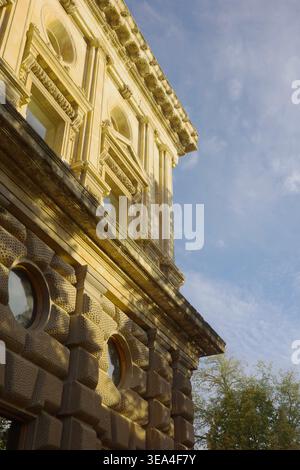 Low-angle view of the Palace of Charles V facade with rusticated stonework, carved reliefs and arched windows in golden sunlight, Alhambra, Granada Stock Photo