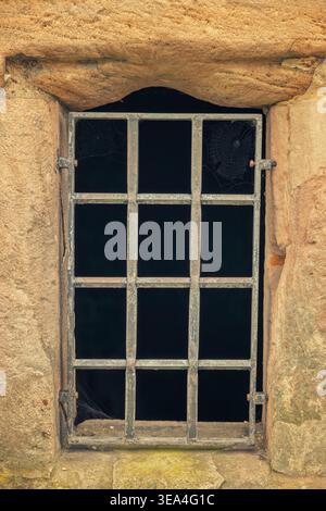 Close-up of a stone wall opening with rusted iron bars and a dark void, featuring an ancient, mysterious atmosphere in a dungeon or castle. Stock Photo