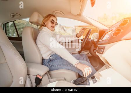 Woman Car Driving Gearshift - A woman in a car, wearing sunglasses and a white sweater, is driving. She is shifting gears while looking straight ahead Stock Photo
