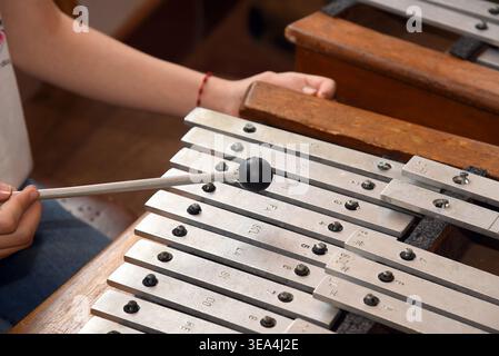 Close-up of a child's hands playing a metallophone with a mallet, focusing on the metal keys with engraved musical notes. Stock Photo