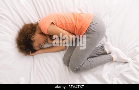 African-american woman curling up in bed, top view Stock Photo
