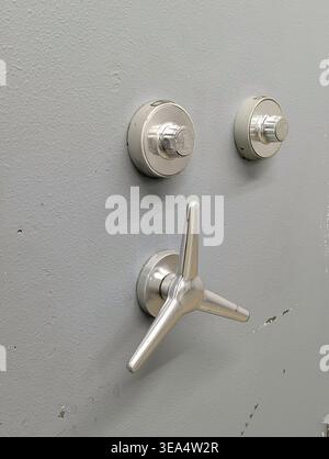 Close-up of a professional bank vault or Secure safe with two mechanical combination locks and a three-spoke chrome handle on a grey metal background. Stock Photo