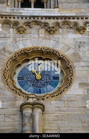 Ornate clock set into historic stone building facade with decorative carvings and Roman numerals on circular dial Stock Photo
