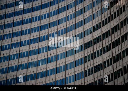 Close-up view of modern office building facade with repeating glass windows and metal panels forming geometric pattern in urban environment. Stock Photo