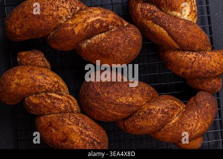 Freshly baked twisted cinnamon rolls cooling on a black wire rack, golden brown and aromatic, perfect for a sweet breakfast or afternoon snack in a co Stock Photo