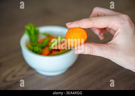 Hand taking carrot vegetable chip from bowl on wooden table. Healthy snack choice and clean eating lifestyle concept. Stock Photo