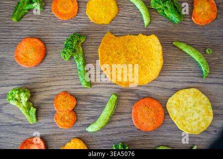 Seamless pattern of vegetable chips with broccoli carrot peas and sweet potato on wooden background. Healthy snack texture and clean eating concept. Stock Photo