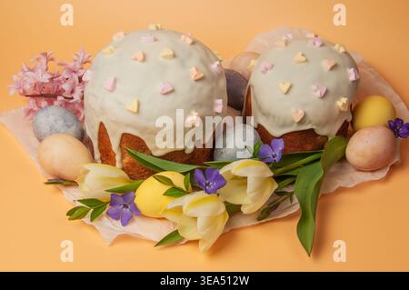 Two beautifully decorated Easter cakes, known as kulich, are surrounded by colorful painted eggs, delicate tulips, hyacinths, and small purple flowers Stock Photo