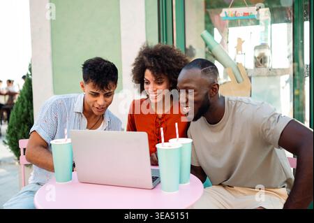 Friends bond through digital experiences, exploring content together on a laptop enjoying technology Stock Photo