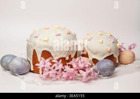 Two beautifully decorated Easter cakes, known as Kulich or Paska, are presented with pastel-colored eggs and delicate pink hyacinth flowers on a white Stock Photo