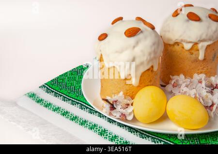 Two beautifully decorated Easter cakes, known as kulich, are presented with vibrant yellow eggs and delicate spring blossoms on a traditional embroide Stock Photo