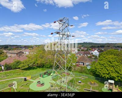 Electricity pylon next to park and playground, carrying electricity to homes, through the residential area of Ferring, West Sussex, England, UK. Stock Photo