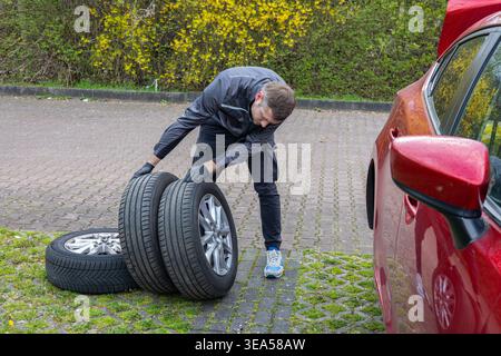 Man changing car tire on parking lot replacing wheel during seasonal maintenance outdoors Stock Photo