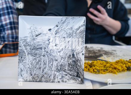 A close up view of a square white plate stained with squid ink after a meal in Valencia, Spain, creating a natural abstract art pattern. Stock Photo