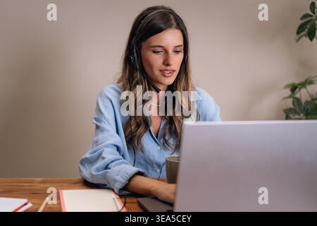 Female customer support agent working remotely with headset and laptop at home. Online meeting, customer service, remote assistance and call center co Stock Photo
