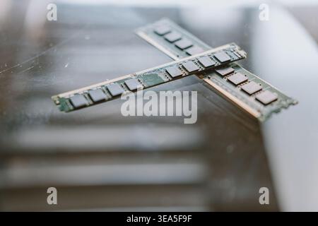 Crossed RAM modules on reflective surface with shallow depth of field, close-up tech hardware shot Stock Photo