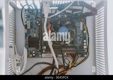Top-down view of computer motherboard with cooling fan, cables, and components inside open white PC Stock Photo