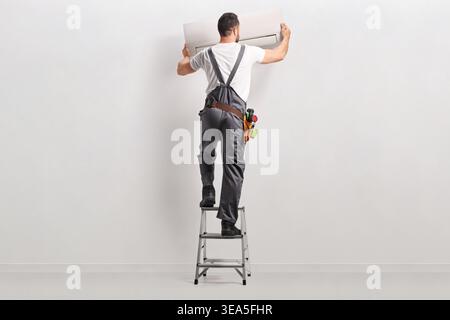 Technician on a ladder installing an air conditioning unit Stock Photo