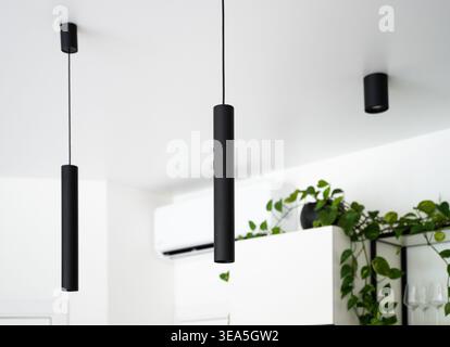 Black minimalist pendant lights illuminating modern interior design with clean white ceiling and green plant details Stock Photo
