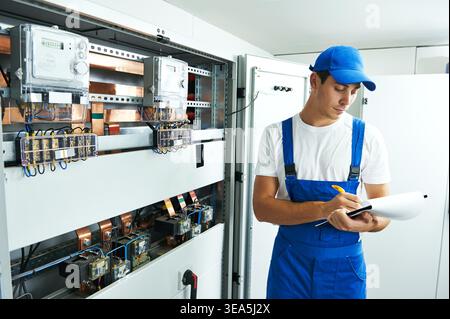 electrician builder engineer inspector checking data of equipment in fuse box with blueprint project Stock Photo