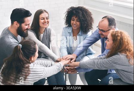 Happy rehab group patients connecting hands at therapy session Stock Photo
