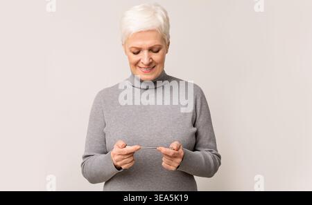 Senior Woman Smiling While Using Smartphone in Cozy Indoor Setting Stock Photo