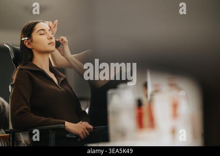 Model receiving makeup application from an artist at a professional beauty center before a shoot Stock Photo