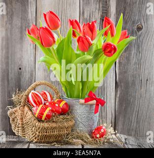 Bouquet of red tulips in a metal bucket in front of a wooden wall with an Easter basket and Easter eggs, still life, cutout Stock Photo
