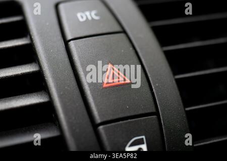 Macro close up of a car hazard light button with a red triangle symbol and dynamic traction control switch on a black dashboard Stock Photo