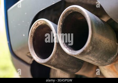 Close up of dual metal exhaust pipes on a modern blue car showing carbon buildup and soot from engine combustion Stock Photo