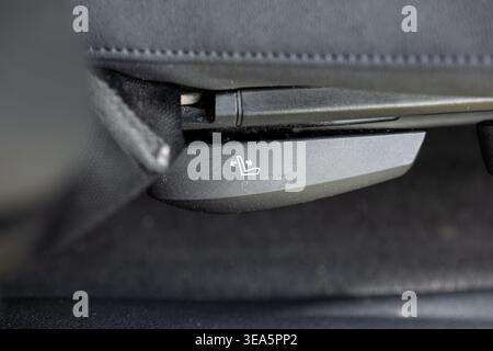 Macro close up of a car seat adjustment lever with a white icon on a black textured plastic base Stock Photo