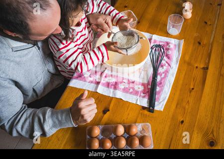 father daughter baking together at home in the kitchen with flour, concept of fatherhood and bonding with children, cooking together with complicity Stock Photo