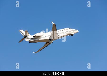 Scenic close bottom view modern luxury expensive white private jet plane dispatching from airport isolated on blue clear sky background. Executive Stock Photo