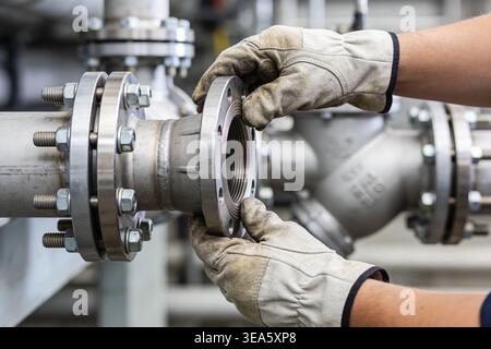 Close-up of a person wearing work gloves connecting two sections of industrial piping using a flanged joint and fasteners Stock Photo