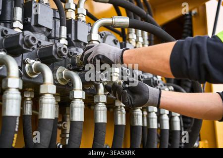 Close-up of a technician's hands in protective gloves working on the complex hydraulic system of industrial equipment Stock Photo