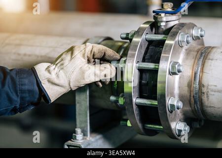 Close-up of a gloved hand using a wrench to secure a bolt on a large industrial pipe flange, highlighting maintenance and construction work Stock Photo