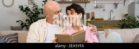 A loving senior couple enjoys a peaceful afternoon cuddling on the couch while reading a book. Stock Photo