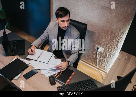 Businessman working at desk reviewing documents and taking notes in modern office Stock Photo