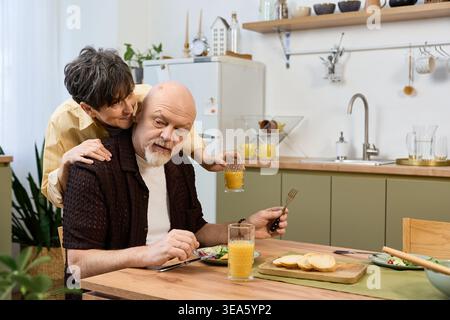 A senior couple shares smiles and breakfast together in their bright kitchen. Stock Photo