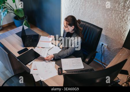 Businesswoman working on team financial reports at her desk with laptop and documents in a modern office Stock Photo