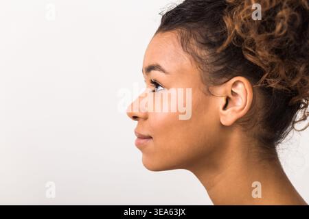 Young Woman With Curly Hair Poses Sideways Against a Plain Background Stock Photo