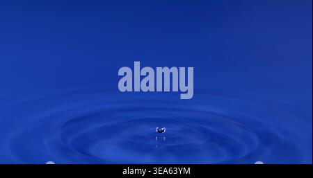 Water droplet causes ripples in blue surface during a drop event Stock Photo