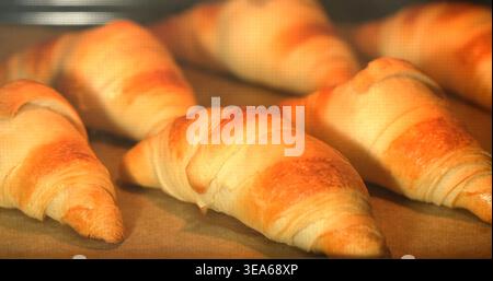 Freshly baked croissants cooling on a baking tray in a kitchen setting during the early morning hours Stock Photo