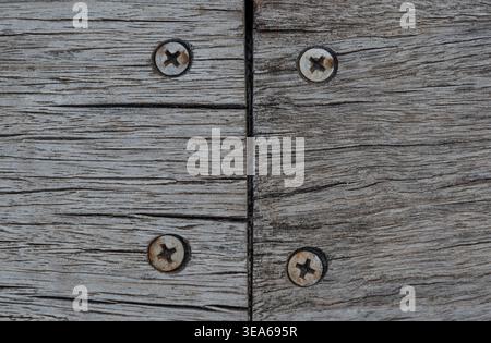 Four rusty metal screws fasten rough textured weathered grey wooden planks together creating a sturdy surface Stock Photo