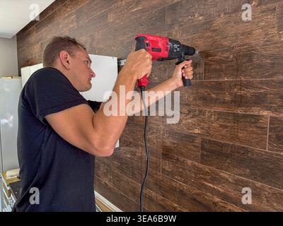 Man drilling wooden wall panel during renovation. Stock Photo