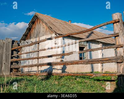 Old farmhouse with wooden fence in rural area under blue sky in daylight Stock Photo