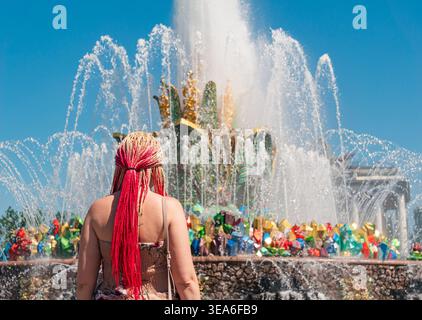 Woman with bright red and blonde braids observes the grand Friendship of Peoples Fountain at VDNKh in Moscow Stock Photo
