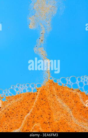 Stream orange sand falling into liquid with bubbles against bright blue background Stock Photo