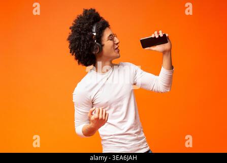 Emotional black guy in wireless headphones singing into phone Stock Photo
